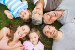 a white family laying down on the grass in a circle with kids, parents, and grandparents